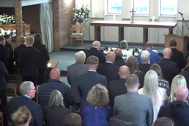 Guests stand at the funeral service as hymns are played aloud.