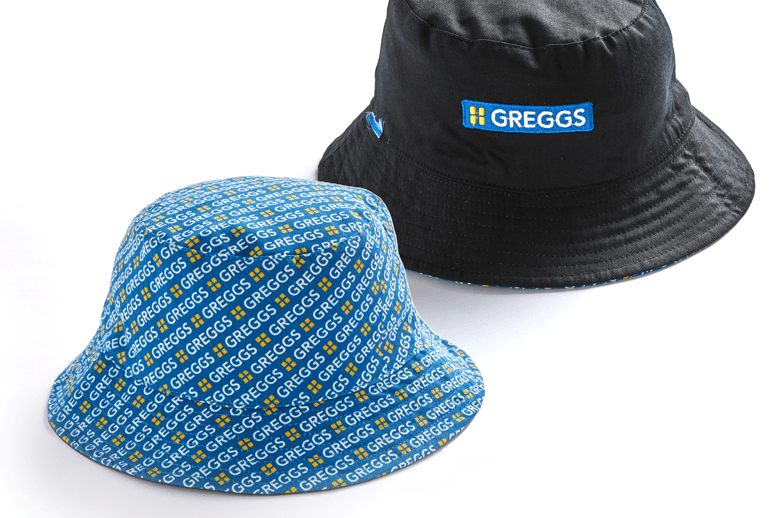 “The Greggs Bucket Hat features a simple black outer design with a reversible blue logo-filled lining. Perfect for festival goers and superfans alike.”