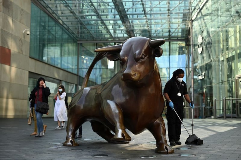 A worker wearing a face mask or covering due to the COVID-19 pandemic, sweeps the floor near a statue of a bull at the Bullring in Birmingham, central England on September 14, 2020 after the British government imposed fresh restrictions on the city after an rise in cases of the novel coronavirus