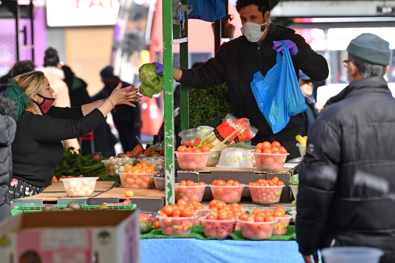 A fruit and vegetable trader wearing gloves and a mask as a precautionary measure against covid-19, serves a customer at a market in Birmingham a day after the nationwide lockdown is announced