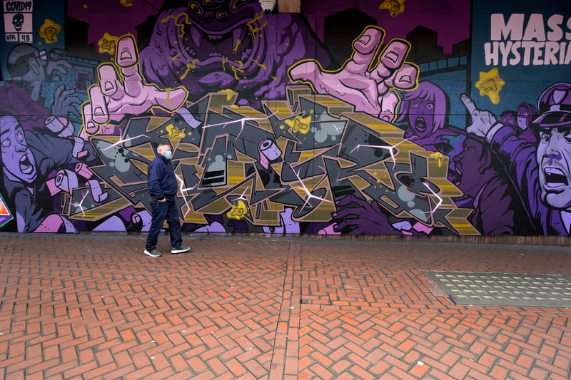 A man wearing a mask walks past Covid-19 themed graffiti in Birmingham city centre during the nationwide lockdownon March 29, 2020