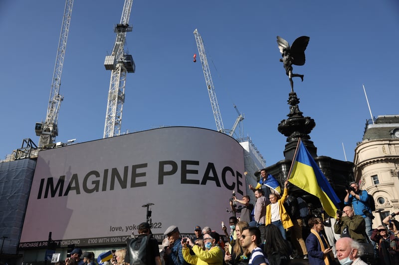 A protestor waves a Ukrainian flag near the ‘Imagine Peace’ slogan by Yoko Ono. Photo: Getty