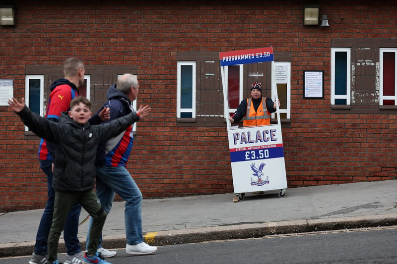 Fans walk past a programme seller ahead of the English Premier League football match 