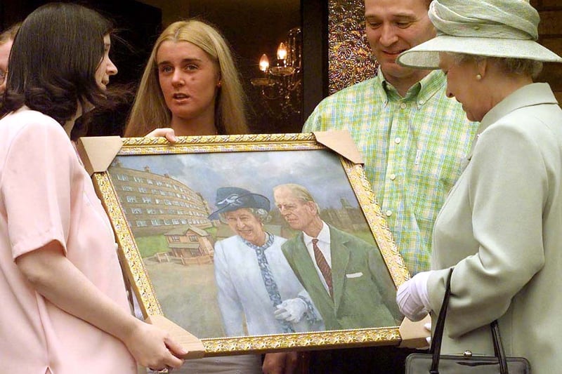 Queen Elizabeth II receives a painting recording her visit with the Duke of Edinburgh to the St. Andrews Gardens Estate, presented by Brenda Prendergast and her husband Charles after she visited their home. The painting includes their home with the Bullring on the left.
