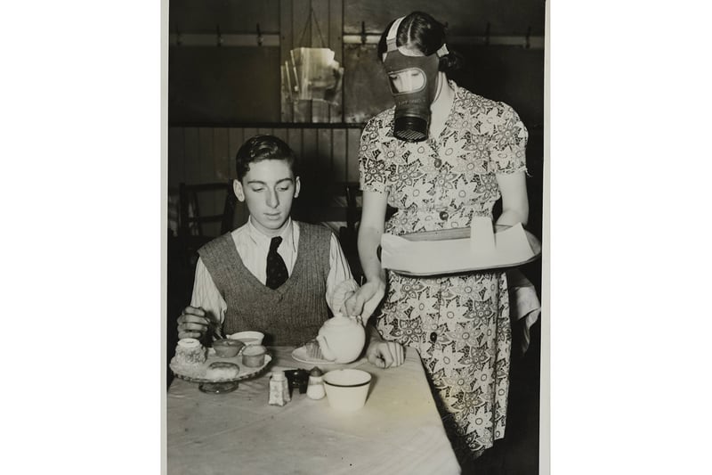 A waitress wearing her gas mask as she served a meal in a cafe, Manchester, England. 