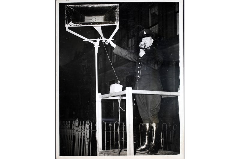A look-out policeman on a platform gives instructions through a loudspeaker to his white-coated colleagues who guide pedestrians over the road in Manchester; December 1939