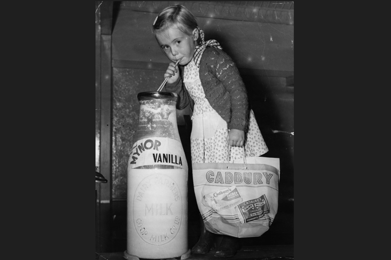 A young girl drinking from an oversized bottle of milk at the Royal Easter Show in Sydney, carrying a bag advertising Cadbury’s chocolate. 