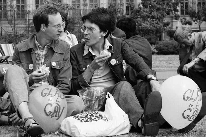Two men picnic in Victoria Gardens by the Houses of Parliament, London, during Pride Week. Their balloons have the slogan ‘Glad to be Gay’. August 5 1976