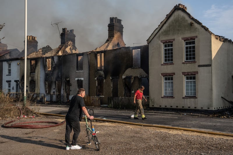 A local councillor looks on as a fireman passes buildings destroyed by fire on July 19 in Wennington. 