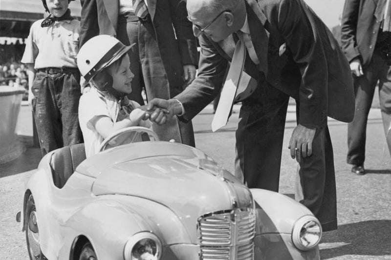 Sir Leonard Lord (1896 - 1967), chairman of the Austin Motor Company, congratulates 8-year-old Alan Swadling on winning the Junior Grand Prix, a race for children of employees at Longbridge, 10th July 1955. The company is celebrating its Golden Jubilee (50 years), and Alan’s prize is the car he is driving. 
