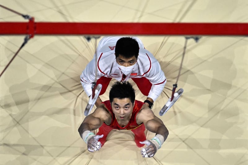 China’s You Hao is helped to grab the rings in order to compete in the Men’s Rings qualification event. (Photo by BEN STANSALL/AFP via Getty Images)