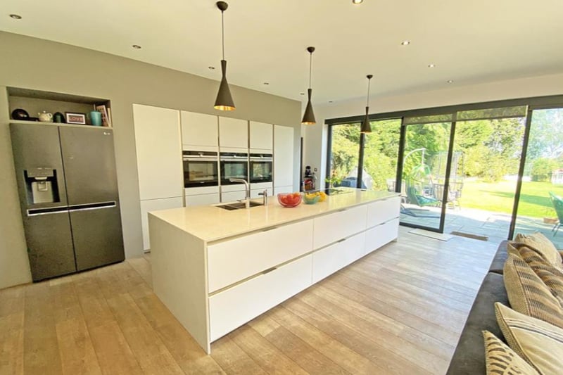 The large, open plan kitchen features modern fitted cabinets and appliances. The large windows open on to the garden.