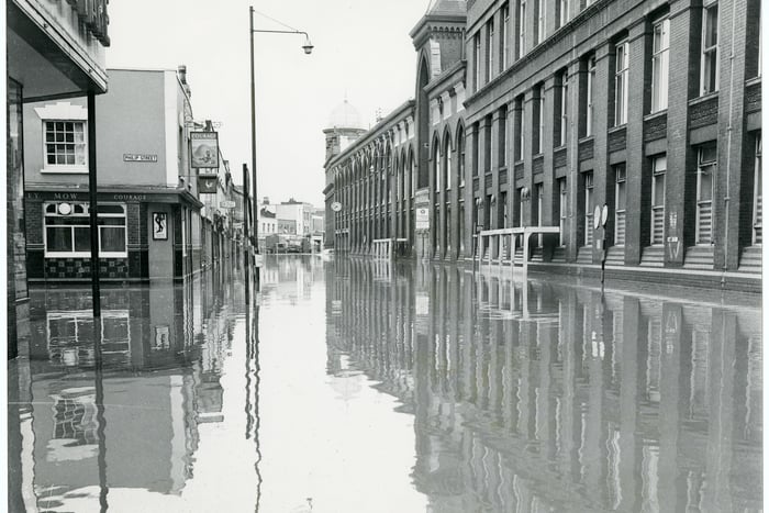 Bedminster Parade under water. Looking down East Street, the Barley Mow pub can be seen on the left. Many shops along the parade and East Street were flooded.  The WD & HO Wills Factory, right, was brought to a standstill, with much of its stock damaged - the end section of the factory would become an ASDA superstore in 1987.