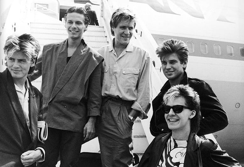 Duran Duran smile and laugh while posing on an airplane ramp before departing for Australia, Heathrow Airport, London, England, July 26, 1983 (Photo by Express Newspapers/Getty Images)