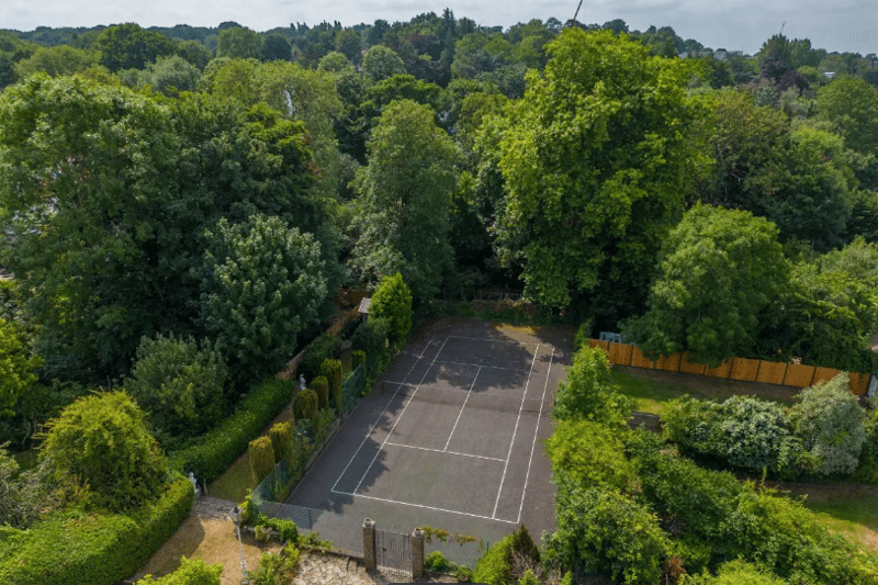 The back of the property with a private tennis court surrounded by tall trees