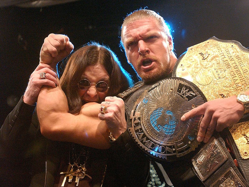 Ozzy Osbourne (L) pretends to bite the arm of pro-wrestler Tripple H at a news conference to announce the lineup for “Ozzfest” 2002 March 21, 2002 at the World Wrestling Federation headquarters in New York. (Photo by Spencer Platt/Getty Images)