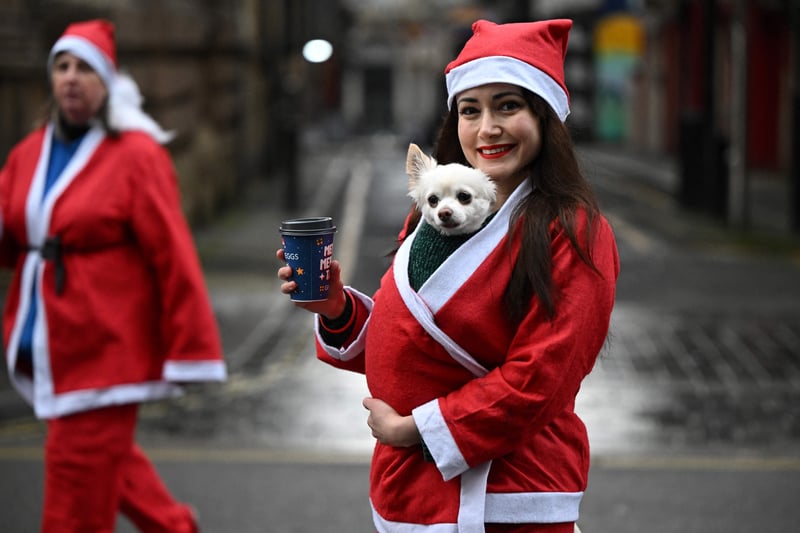 A runner dressed in Father Christmas attire carries her dog. (Photo by OLI SCARFF/AFP via Getty Images)