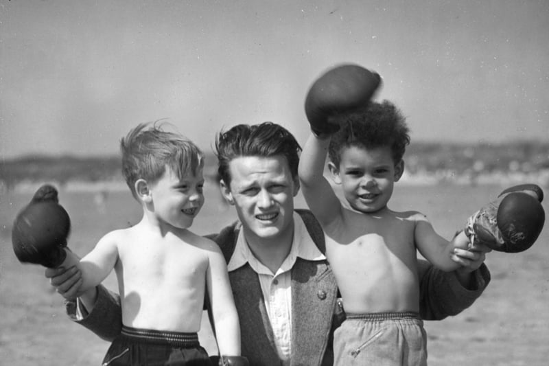 12th July 1954:  Chris Davies, leader of the United Nations Boys’ Club in Wirral, Merseyside, gives young Billy Feston and Paul Wilson a boxing lesson on the beach. Image: Kenny Rhodes/Fox Photos/Getty Images