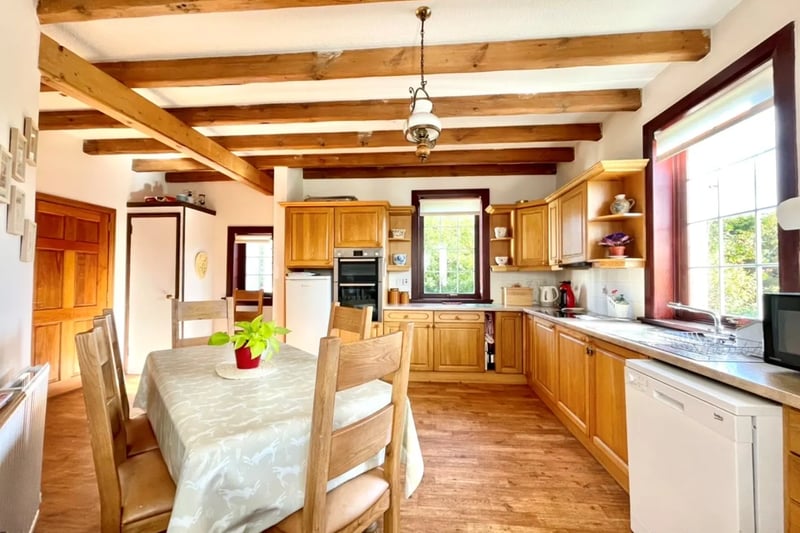 This traditionally styled kitchen/dining room with feature wooden beams has ample storage units at base and wall levels, worktops, splash back tiling and stainless steel sink and drainer.