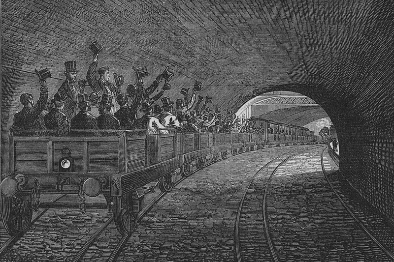   Commuters waving their hats in the air as they pass Portland Road station during a trial trip on the London Metropolitan Underground railway in 1863