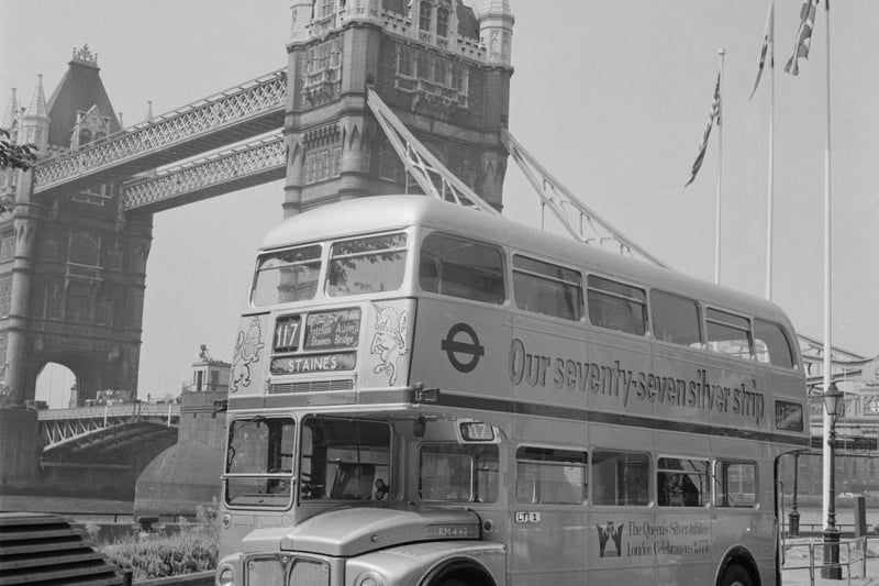 A double-decker bus in livery commemorating the Silver Jubilee of Queen Elizabeth II, on the Thames Embankment with Tower Bridge rising beyond, in London, England, July 1976. (Photo by Evening Standard/Hulton Archive/Getty Images)