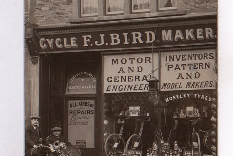Two men in a motorcycle and sidecar are pictured outside of the entrance to the shop. The picture is from 1919. The shop is now a tattoo parlour, although there is a bike shop today at 12 Sandy Park Road.