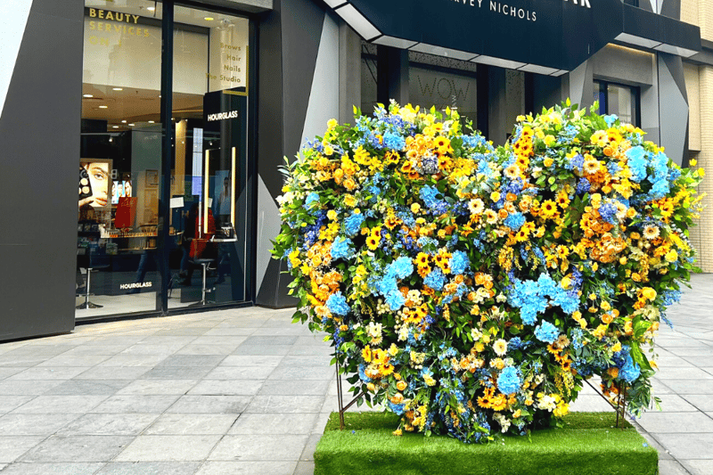 A yellow and blue floral heart display is placed outside Waterstones and Beauty Bazaar.