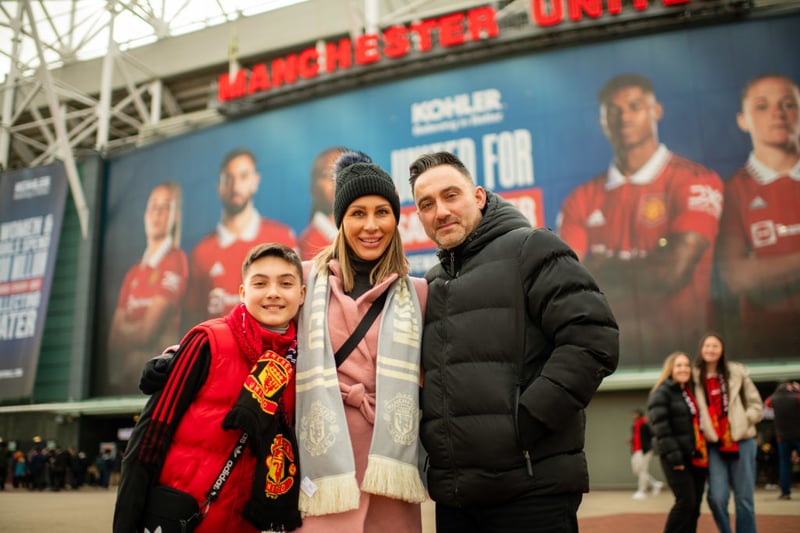 A family pose for a photo outside of Old Trafford with large images of Ella Toone and Ona Batlle in the distance.