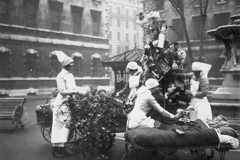 December 23 1929:  Nurses at St Bartholomew’s Hospital in London distributing toys to young patients using a portable Christmas tree which can be wheeled around the hospital grounds.  (Photo by Puttnam /Topical Press Agency/Getty Images)