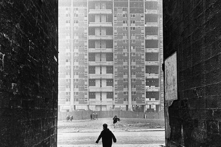 A child snapped mid-run down an alleyway in the Gorbals - a crane can be seen constructing a high-rise block of flats in the background. 