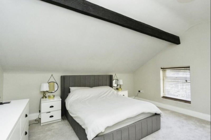 The large master bedroom has wooden beams and a lush carpet.