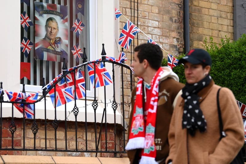 Liverpool fans walk past a house decorated for the coronation prior to the Premier League match between Liverpool FC and Tottenham Hotspur at Anfield.