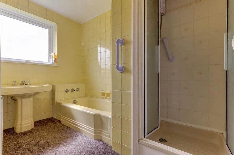 A dated bathroom is spacious and has both a bath and a shower