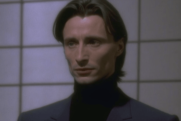 Robert Carlyle wearing a sleek, all-black suit with a matching turtleneck sweater and black leather ankle boots