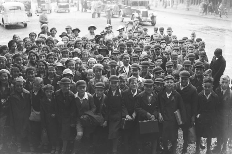 The children on this school outing can barely hide their excitement as they prepare to go inside the station with their teachers smiling in the background. Date is 1936.