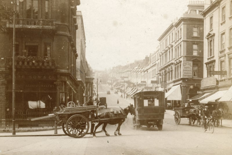 An early 20th Century view looking up Park Street with a shop front displaying a full-sized horse advertising blankets and tack. An early motor bus heads up the hill towards Clifton.