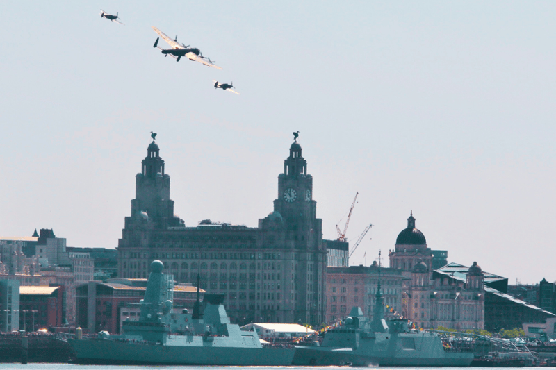 A Lancaster Bomber, Spitfire and Hurricane fly over HMS Defender and French Navy frigate Bretagne docked in Liverpool.