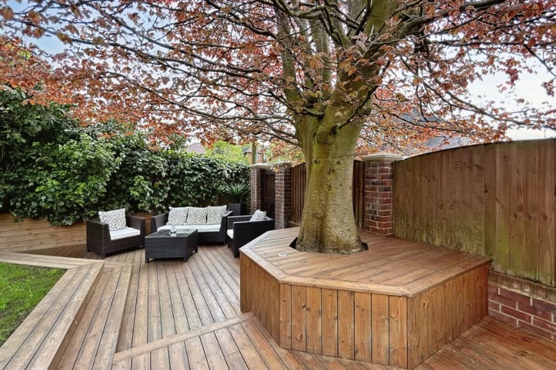 In the corner of the garden is a gorgeous seating area underneath a large tree