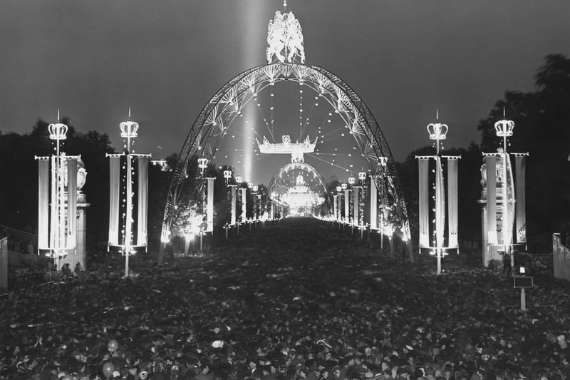 A crowd of people and beneath illuminations on The Mall during the celebrations that followed the Coronation of Elizabeth II, in Westminster, London, England, 2nd June 1953