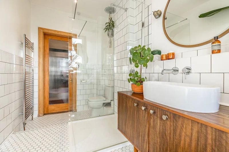 Refitted shower room with glass shower cubicle, toilet and wash hand basin set upon a mid-century dresser. 