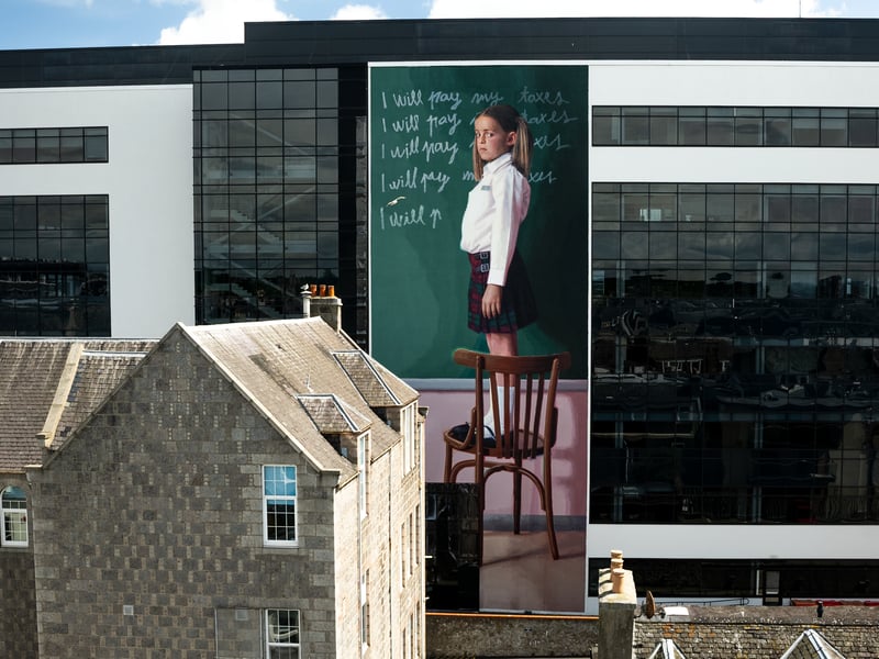 Titled “The Punishment”, Spanish artist Slim Safont’s striking mural is certainly among not just Nuart Aberdeen’s best, but the world, coming in at number 4 in Street Art Cities Best of 2022 list. Featuring a young schoolgirl writing lines on a chalkboard, Safont’s artwork represents the indoctrination mechanisms used from a young age to keep us under control and direct our lives towards pre-established models – with the lines reading “I will pay my taxes”. This standout artwork is in good company at Union Plaza, where it looms over pedestrians.