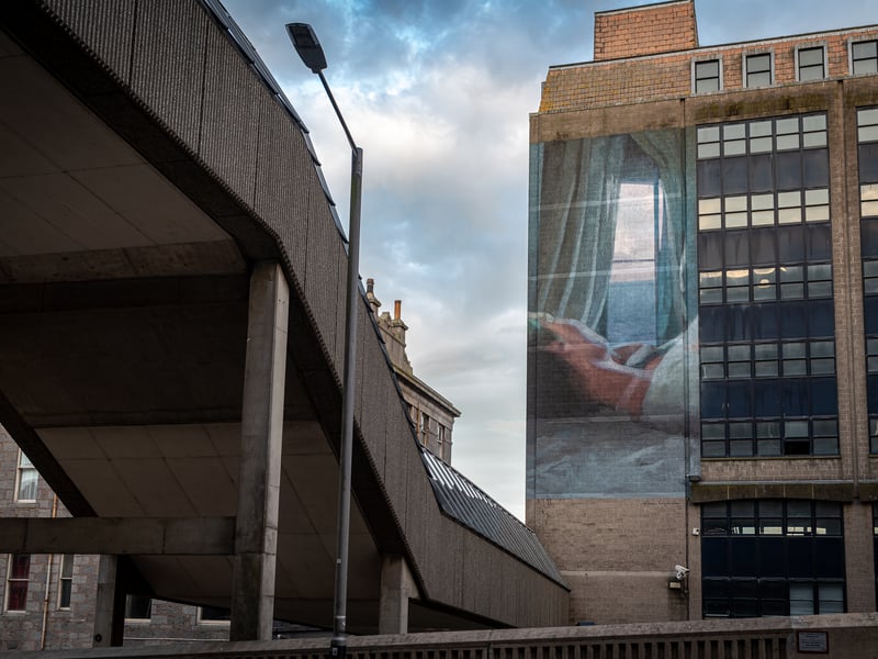 Emotive from first glance, Elisa Capdevila’s 2022 Nuart mural is a window into the life of a woman who is spending time alone at home. Featuring a woman gazing out of an open window, and based on a photograph her partner took, Spanish artist Capdevila slots neatly into its surroundings. It can be easily viewed from Wapping Street and if you’re walking down the Trinity Centre’s stairs to reach Union Square.