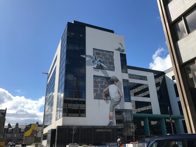 Considering this mural was installed as part of a street art festival, artist Ernest Zacharevic’s background as a classically trained painter with a degree in fine art may come as a surprise. Born in Lithuania, Zacharevic’s mural of a child climbing the modern Union Plaza office building helps make the spot feel more human. A popular area for Nuart work, tucked just off Union Street, the Plaza has become home to many murals over the years.
