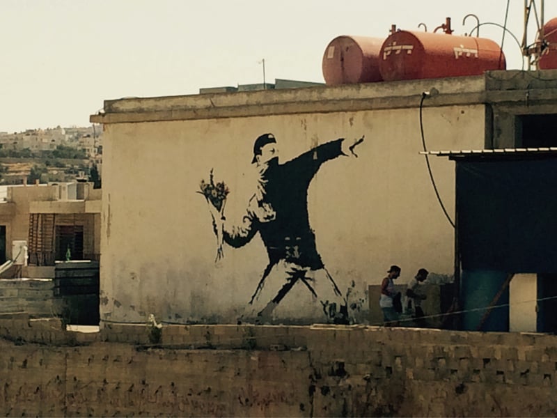 Widely considered to be the street artist’s most famous work, the “flower thrower” was painted in Jerusalem on the wall that separates Palestine from Israel. It depicts a man tossing flowers over the wall in a pose reminiscent of throwing a molotov cocktail. It is said to represent the artist’s wish for peace between their peoples.