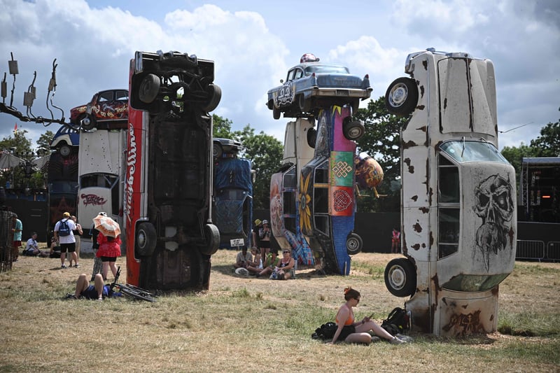 Festivalgoers relax beside the "Carhenge" installation created by underground artist Joe Rush on day 3 of the Glastonbury. (Photo by Oli SCARFF / AFP) 