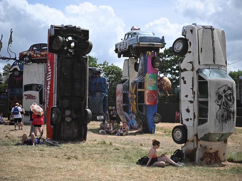 Festivalgoers relax beside the "Carhenge" installation created by underground artist Joe Rush on day 3 of the Glastonbury. (Photo by Oli SCARFF / AFP)