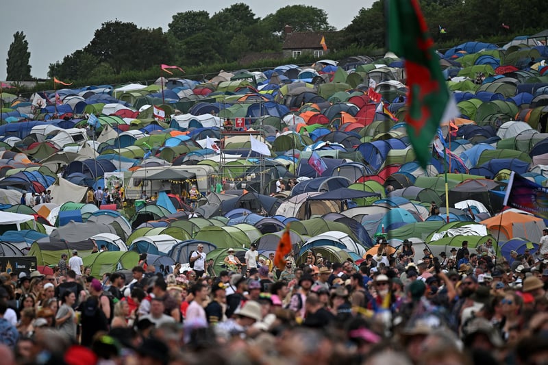 Tents are pictured beyond festivalgoers waiting to hear bands perform on the Pyramid Stage on day 3 of the Glastonbury festival. (Photo by OLI SCARFF/AFP via Getty Images)
