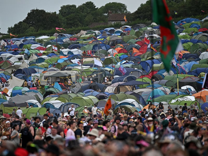 Tents are pictured beyond festivalgoers waiting to hear bands perform on the Pyramid Stage on day 3 of the Glastonbury festival. (Photo by OLI SCARFF/AFP via Getty Images)
