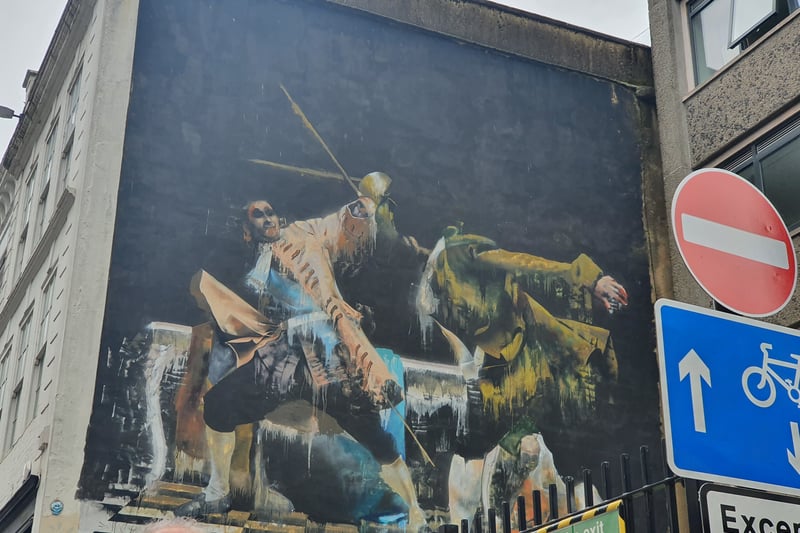 "The Duel of Bristol" is an oil painting mural by Irish artist Conor Harrington made using an art style from Italy's 1560s. Conflict is a common theme in his work and this piece appears to represent the conflict between Ireland and the UK, for example, in the Irish flag between the right figure's legs."