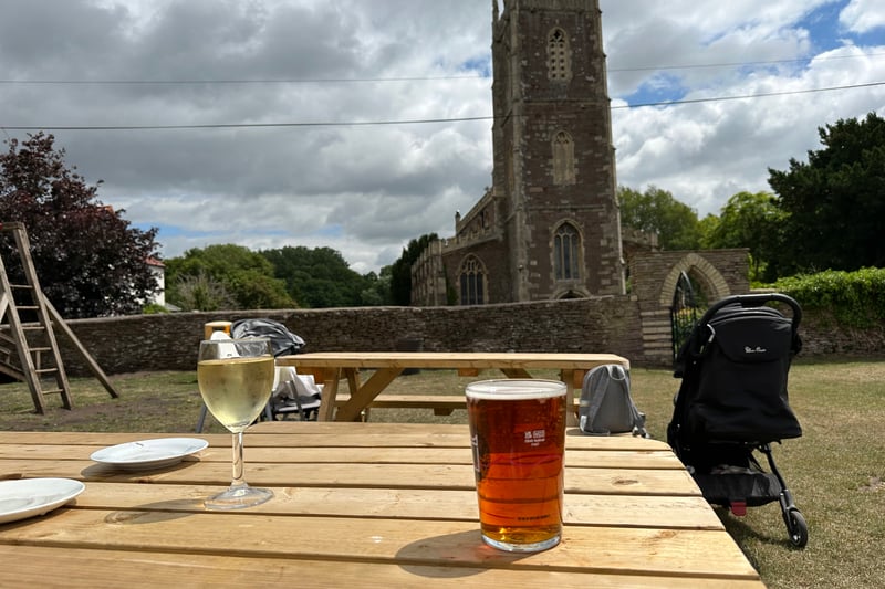 A pint of Pigs Ear from Uley Brewery and a Savagnin Blanc are the focus with the pretty St Peter’s Church in the background behind the garden’s stone wall.